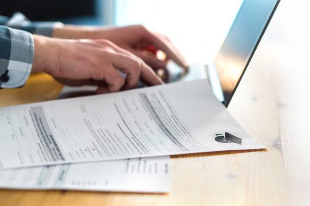 Young man writing college or university application form with laptop. Student applying to school. Scholarship document, admission paper or letter on table. 输入电子邮件. Education and communication.